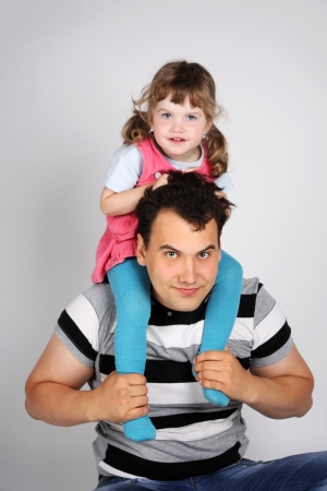 Llittle cute daughter sits on shoulders of his father on grey background.の写真素材