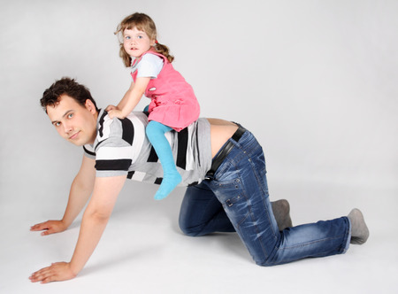 Llittle cute daughter sits on back of his father on grey background.の写真素材