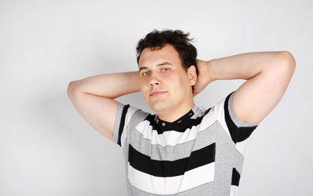 Brunet man in striped T-shirt smiles and stretches oneself on grey background.の写真素材
