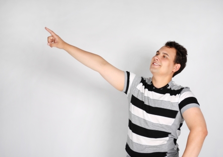 Brunet man in striped T-shirt smiles and points to side on grey background.の写真素材
