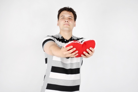 Suffering handsome man gives red soft heart on grey background. Focus on heart.の写真素材