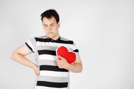Sad enamored handsome man holds red soft heart on grey background.の写真素材