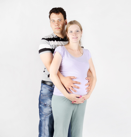 Handsome man hugs belly of pregnant woman on grey background.の写真素材