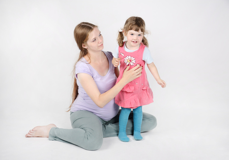 Pregnant woman sits on floor near little smiling daughter on grey background.の写真素材