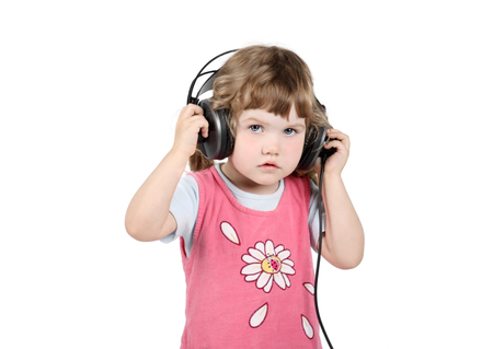 Little girl listens to music in big headphones and looks at camera isolated on white background.の写真素材