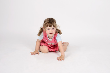 Little smiling barefoot girl in pink creeps on floor and looks away on white background.の写真素材