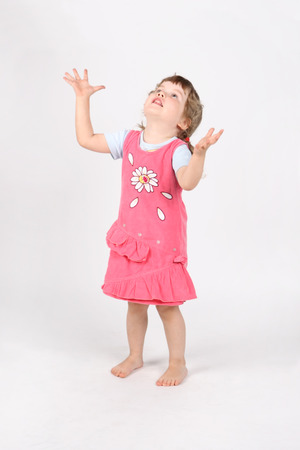 Little barefoot girl in pink with raised hands looks up on white background.の写真素材