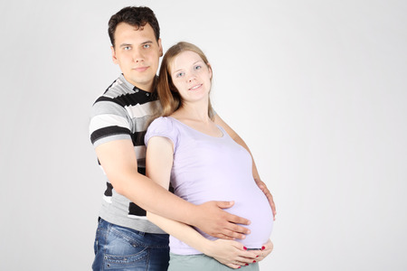 Handsome man embraces belly of happy pregnant woman on grey background.の写真素材