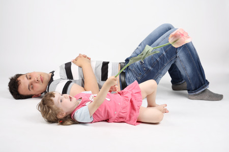Happy father and talking little daughter with flower lie on floor on white background. Focus on girl.の写真素材