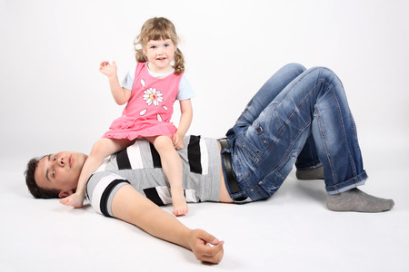 Happy father lies on floor and little happy daughter sits on his chest on white background.の写真素材