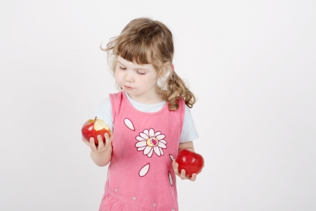 Little beautiful girl in pink eats apple and holds second apple in hand on white background.の写真素材
