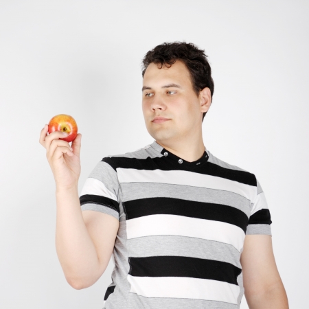 Brunet handsome man holds apple and looks at it on white background.の写真素材