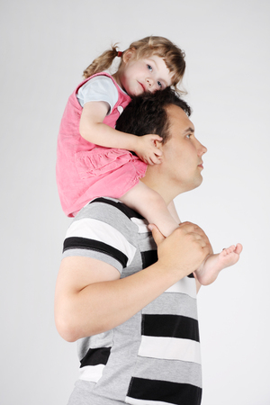 Little cute girl sits on shoulders of her father on grey background.の写真素材
