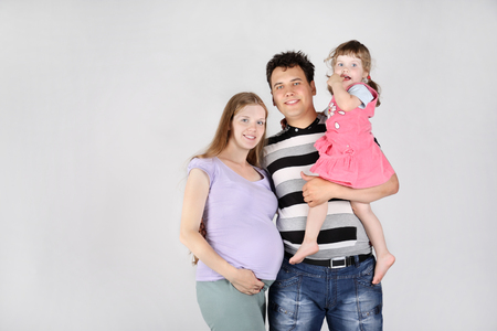 Pregnant mother, happy father and daughter on grey background.の写真素材
