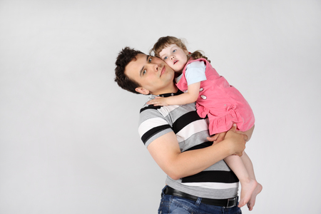 Happy father holds and hugs her little cute daughter on grey background.の写真素材