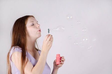 Beautiful woman with long hair blows soap bubbles on grey background.の写真素材
