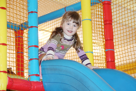 Little cute girl on blue plastic slide on indoor playground.の写真素材
