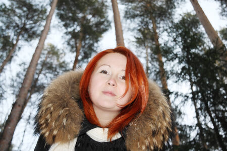Happy redhead girl looks at camera in pine forest at winter.の写真素材