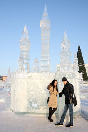 Young beautiful couple stand neat ice castle at sunny winter day  の写真素材