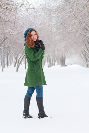 Pretty girl in green overcoat stands outdoor at winter day in parkの写真素材