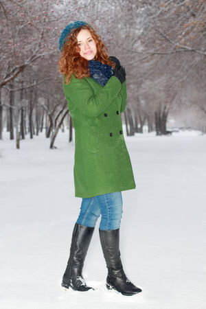 Pretty smiling girl in green overcoat poses outdoor at winter day in parkの写真素材