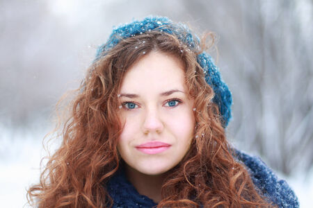 Beautiful girl in blue beret looks at camera outdoor at winter day in parkの写真素材