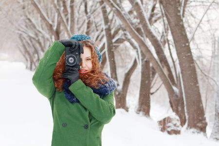Beautiful girl holds photographs by retro camera at winter day in parkの写真素材
