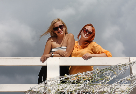Two happy girls in sunglasses stand on white bridge at summer dayの写真素材