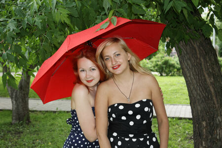 Two beautiful girls with red umbrella stand in park at summer dayの写真素材