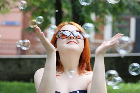 Pretty smiling girl in sunglasses catches soap bubbles in park at summer dayの写真素材