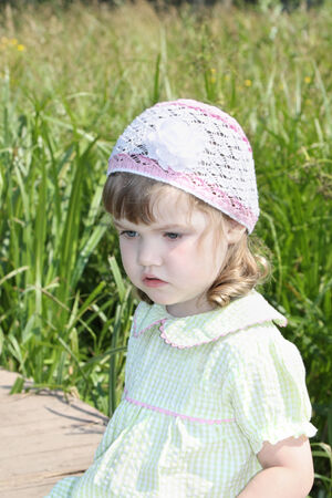 Pretty little girl sits and look away bridge in village at summer sunny dayの写真素材