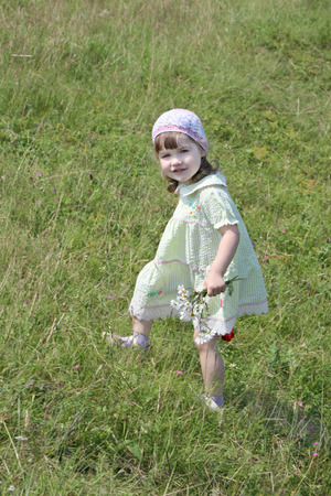 Pretty little girl in dress with flowers walks at meadow at summer sunny dayの写真素材