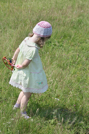Back of pretty little girl in dress with windmill standing at meadow at summer sunny dayの写真素材
