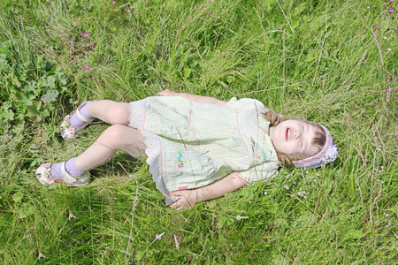 Cute little girl with closed eyes lies on grass of green meadow at summer sunny dayの写真素材