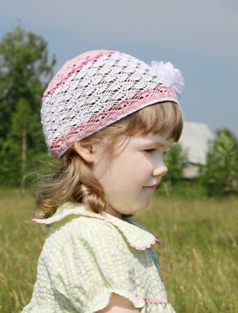 Smiling little girl looks away at meadow near village at summer sunny dayの写真素材