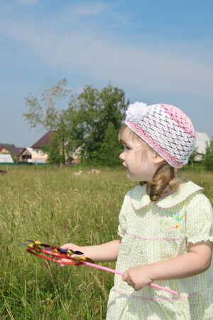 Little girl with windmill looks away at meadow near village at summer sunny dayの写真素材