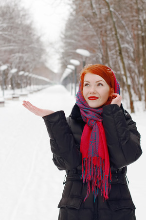 Pretty happy girl in red kerchief catches snowflakes outdoor at winter day in parkの写真素材