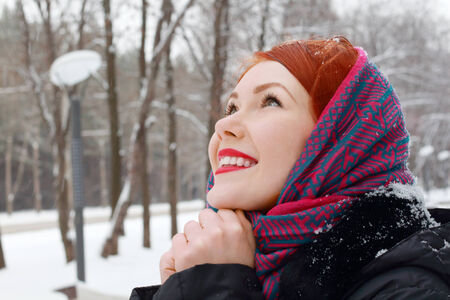 Pretty girl in red kerchief with clasped hands looks up outdoor at winter day in parkの写真素材