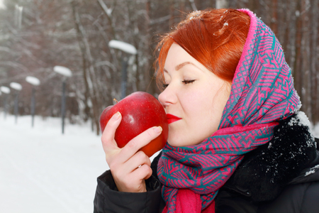 Pretty girl in red kerchief holds big red apple outdoor at winter day in parkの写真素材