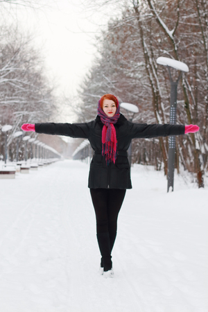 Beautiful girl in black goes with outstretched arms outdoor at winter day in parkの写真素材