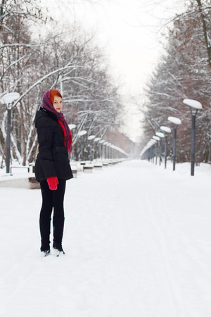 Beautiful girl in black stands and smiles outdoor at winter day in parkの写真素材