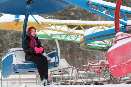 Beautiful girl sits on old carousel outdoor at winter day in parkの写真素材