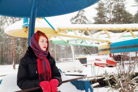 Beautiful girl sits on old carousel and look away outdoor at winter day in parkの写真素材