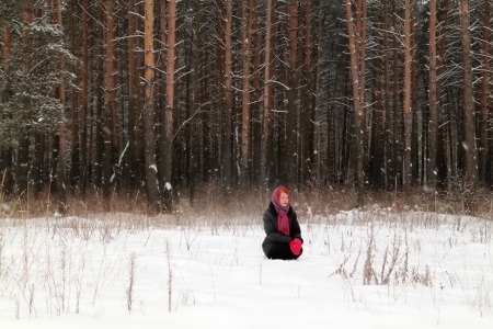 Beautiful girl sits on snow and looks away outdoor at winter day in forestの写真素材