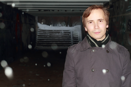 Young man in black stands in small tunnel at winter night during snowfallの写真素材
