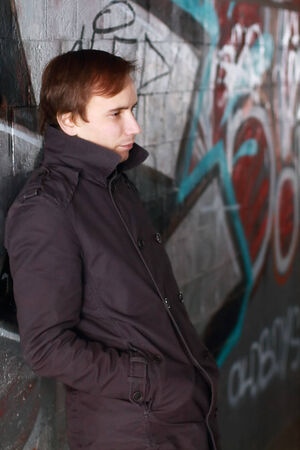 Young man leans back on wall with graffiti and looks aside outdoorの写真素材
