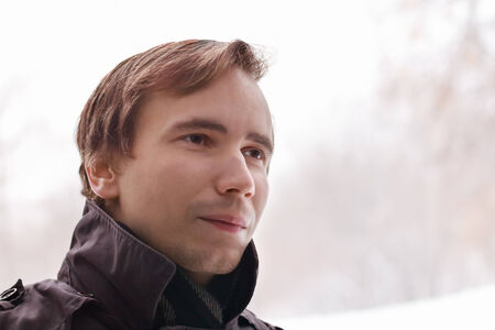 Young unshaven man in back looks away outdoor at winter snowy dayの写真素材