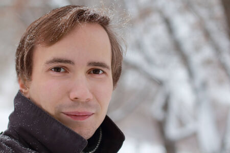 Young unshaven man in back looks at camera outdoor at winter snowy dayの写真素材