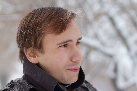 Young unshaven man with snowflakes in hair looks away outdoor at winter snowy dayの写真素材