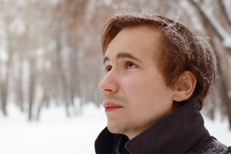 Young man with snowflakes in hair looks up outdoor at winter snowy dayの写真素材